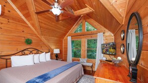 A cozy wooden cabin bedroom with a bed, a desk, a mirror, and a ceiling fan. - Very Private with Incredible Mountain Views! Free Pool and Putt Putt Access! (Sevierville)