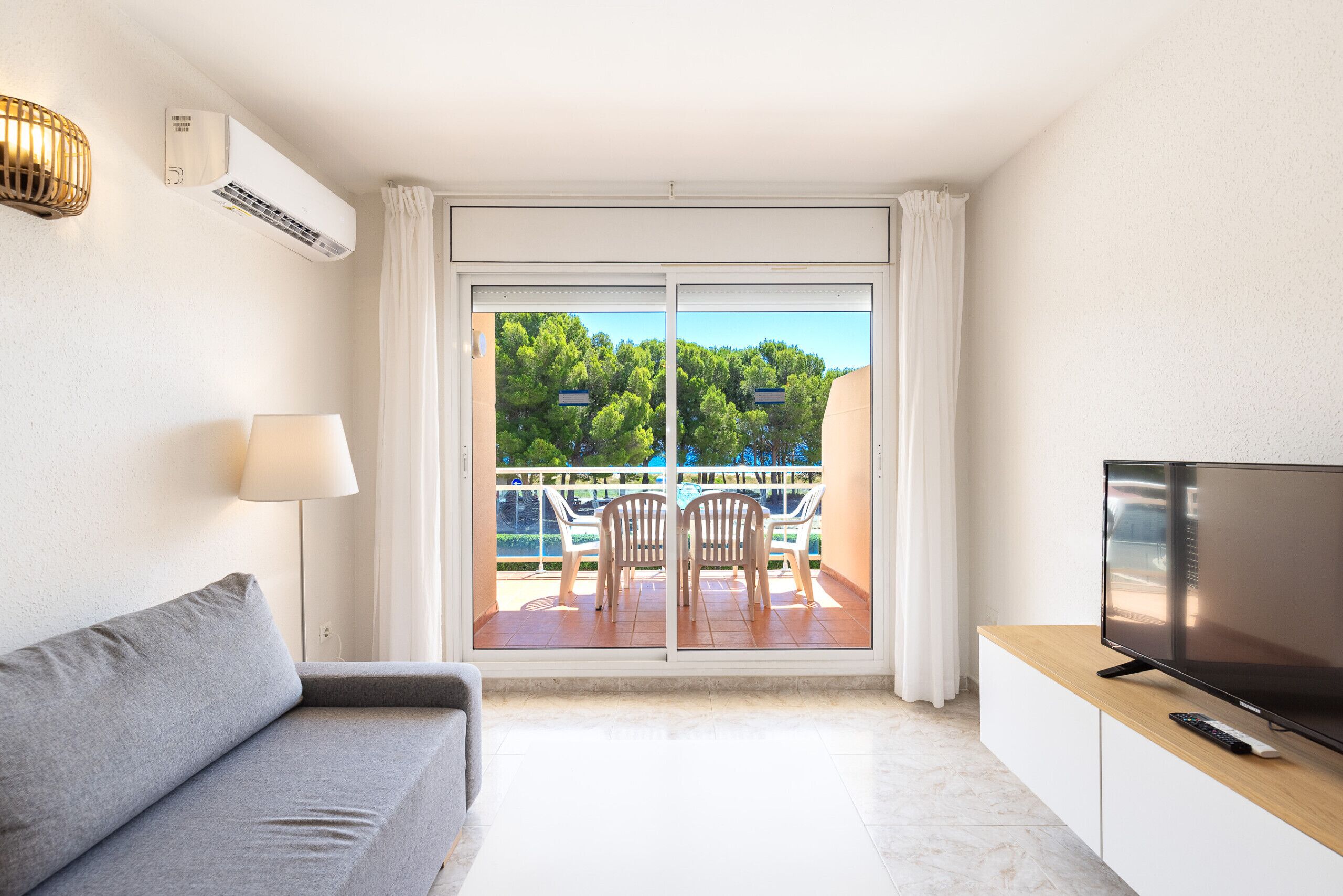 Una sala de estar moderna con un sofá, televisión y un balcón con sillas.