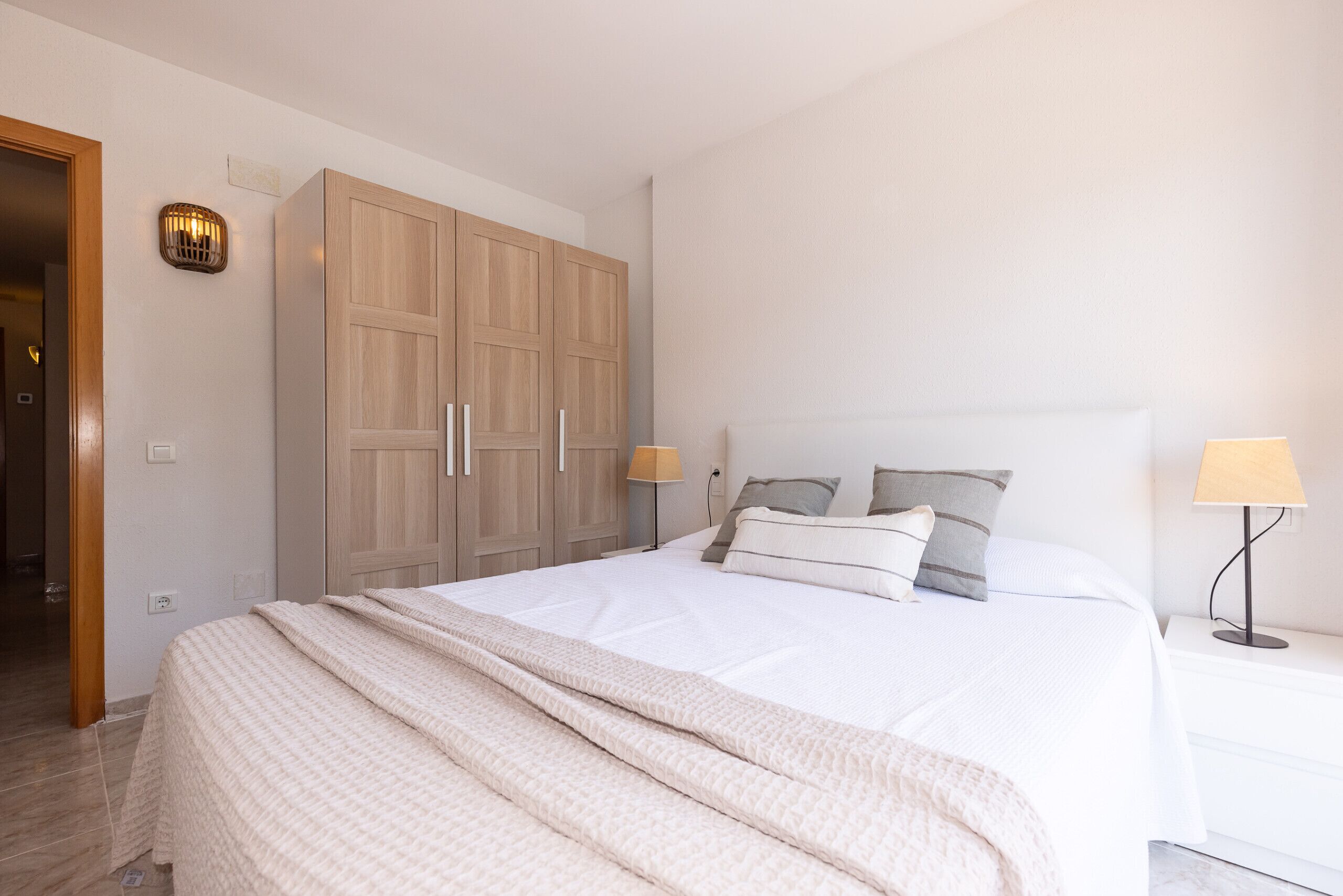 Un dormitorio con cama, lámparas de noche, un armario y una lámpara fijada a la pared.