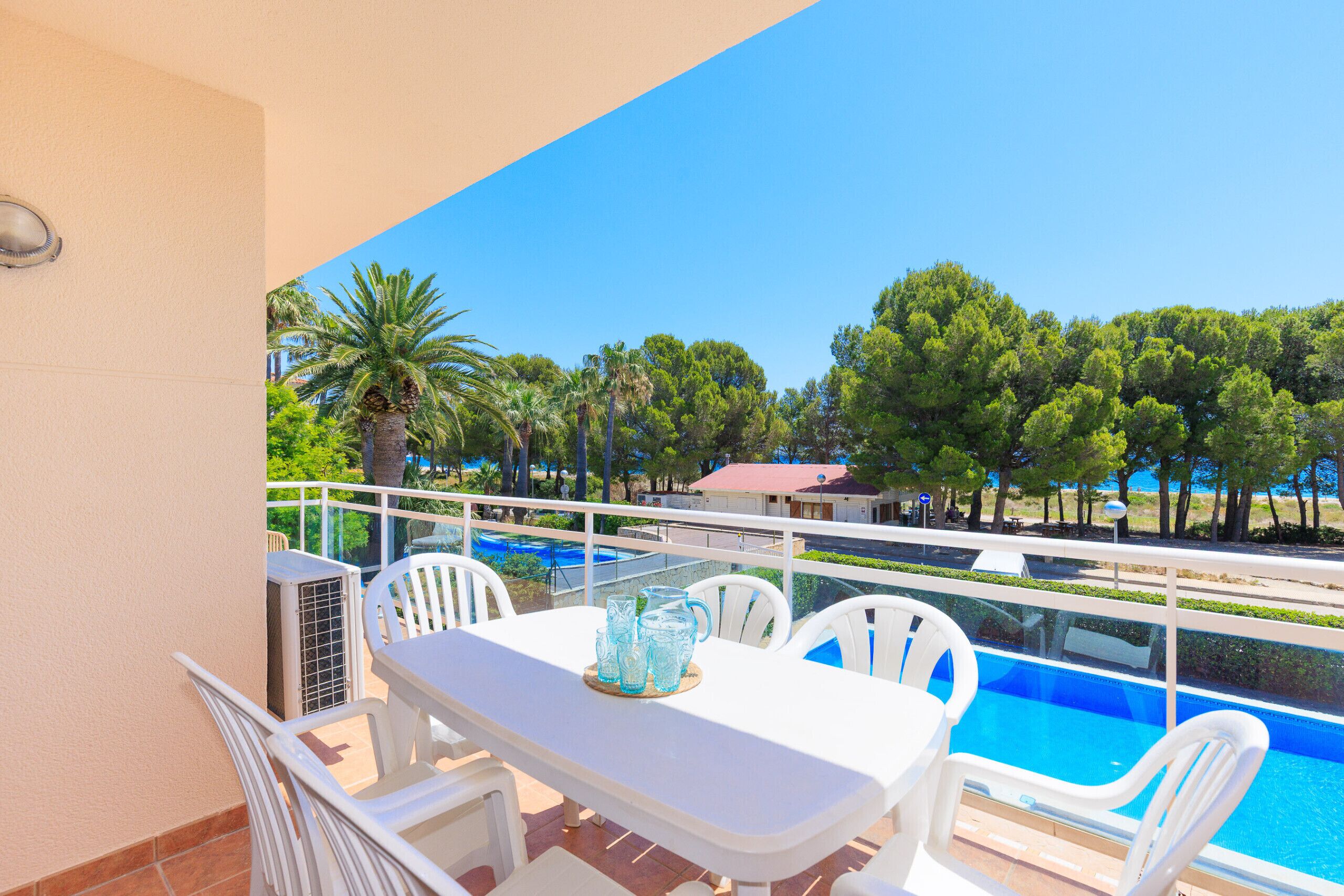 Un balcón con mesa y sillas, con vistas a una piscina y árboles.