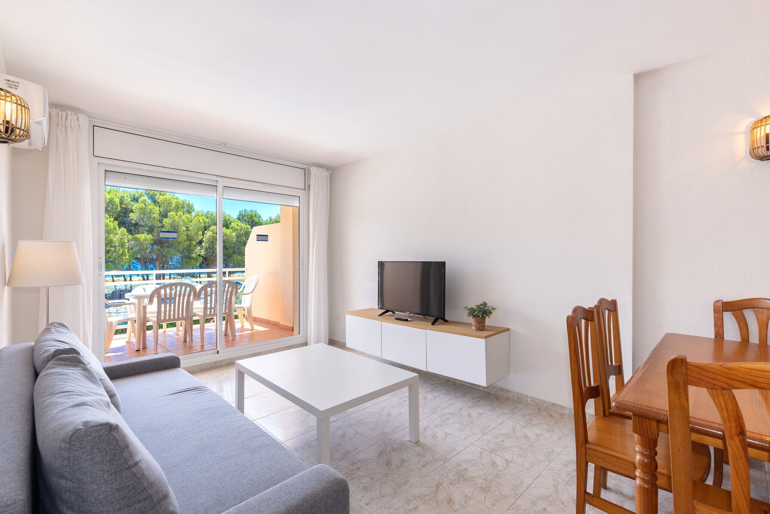 Ein modernes Wohnzimmer mit Sofa, Couchtisch, Fernseher auf einem weißen Schrank und einem Esstisch mit Stühlen.