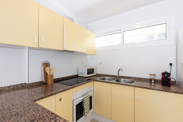 Une cuisine avec des meubles de couleur jaune, un four à micro-ondes, un évier, une cuisinière et une fenêtre.