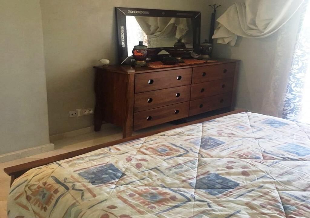A bedroom with a bed, a wooden dresser, and a mirror.