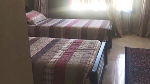 A room with two beds, each with a striped bedspread, a window with sheer curtains, and a patterned rug on the floor. - Beautiful apartment in River Palm 4397 (Marrakech)