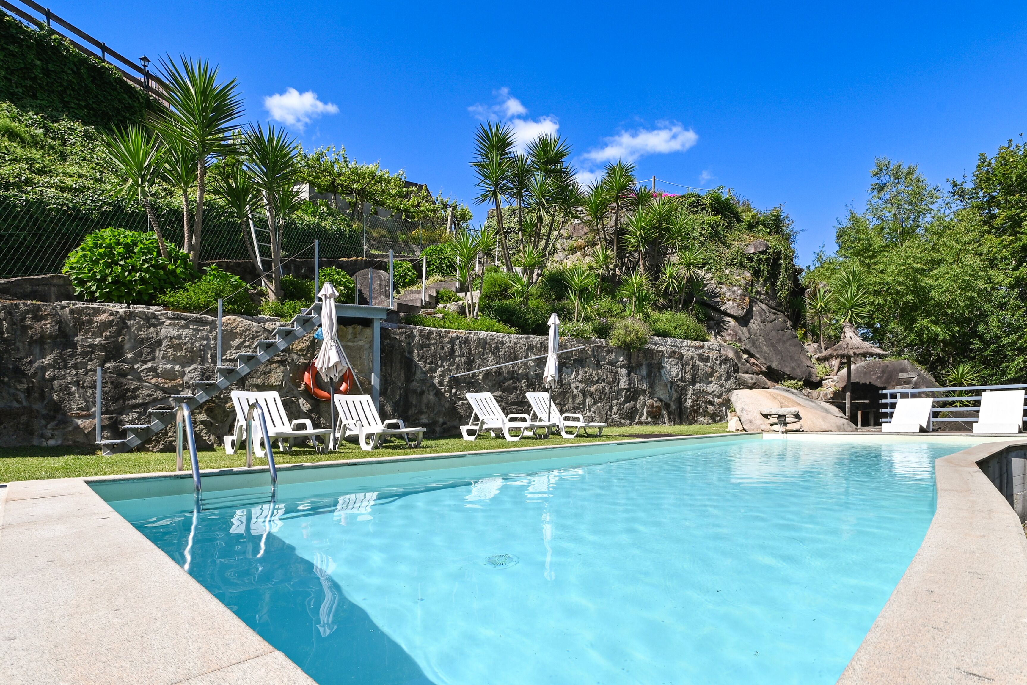 Ein Schwimmbecken mit weißen Liegestühlen und einer Steinwand.
