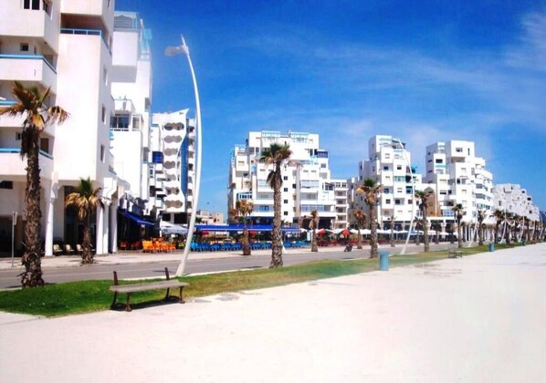 A coastal urban area with modern buildings, palm trees, and a clear sky.