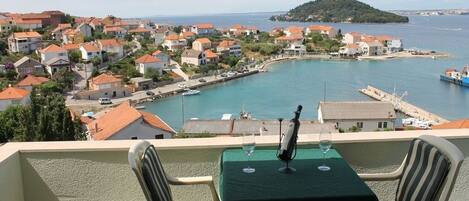 A balcony with a table set for two, overlooking a coastal town with houses and a marina.