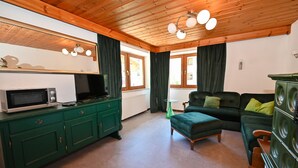 Una sala de estar acogedora con un sofá verde, techo de madera y una zona de cocina con microondas.