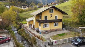 Un edificio amarillo con balcón, una cascada pequeña y montañas al fondo.