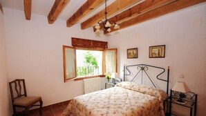 Ein Schlafzimmer mit einem Bett, einem Sessel, einem Fenster mit Vorhängen, einer Heizung und einer Lampe auf einem Nachttisch.