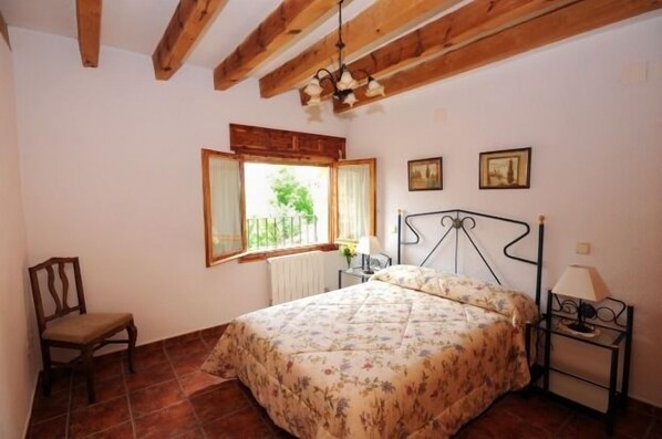 Une chambre à coucher avec un lit, une chaise, une fenêtre avec des rideaux, un radiateur et une lampe sur une table de chevet.