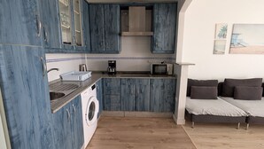 Cozinha compacta com armários azuis, máquina de lavar e área de refeições com sofá.
