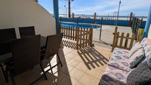 Um pátio ensolarado com piscina, cerca de madeira e vista para a praia.