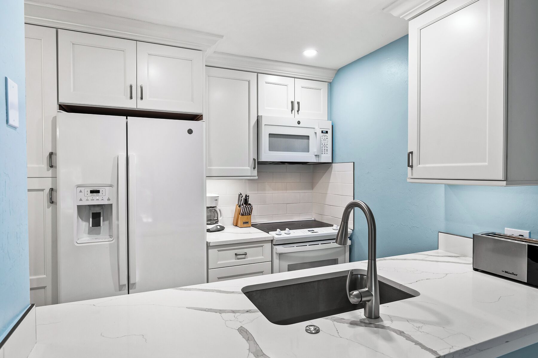 A modern kitchen with white cabinetry, a built-in microwave, a coffee maker, and a sink with a faucet.