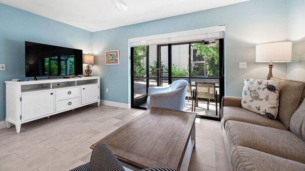 Ein Wohnzimmer mit Fernseher, Sofa, Couchtisch und einem Balkon mit Blick auf Grünflächen.