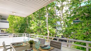 An outdoor dining area with a table set for two, surrounded by a white railing, overlooking a lush green garden. - AirCon Apartment with Pool · Beach 100m · Parking · RUISEÑORES (Salou)