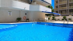 A swimming pool with a clear blue water, surrounded by a white building with balconies and potted plants. - AirCon Apartment with Pool · Beach 100m · Parking · RUISEÑORES (Salou)