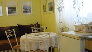 Une petite cuisine avec une table et des chaises, un réfrigérateur et une fenêtre avec des rideaux.