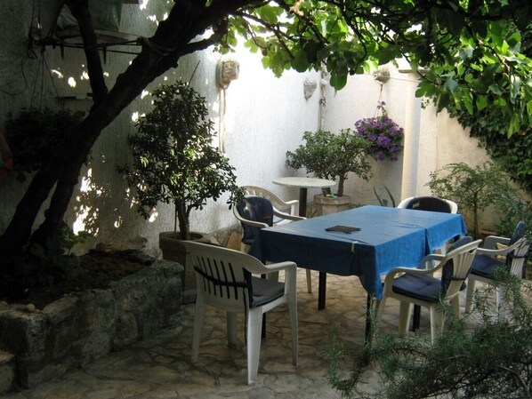 Un patio al aire libre con una mesa y sillas, rodeado de plantas y un muro de piedra.