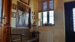 Une pièce avec un banc en bois, un radiateur, une fenêtre avec des stores et une lampe.