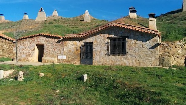 Un bâtiment en pierre, doté d’un toit en tuiles, entouré de terrains couverts d’herbe et d’autres constructions similaires sur le flanc d’une colline.