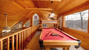 Un interior de madera con mesa de billar, barandillas de madera y grandes ventanales.