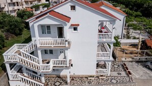 A multi-story white building with a red roof, multiple balconies, and a tiled patio area.