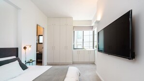 A modern bedroom with a large bed, a TV mounted on the wall, and a walk-in closet.