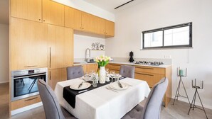 Una cocina moderna con armarios de madera, horno empotrado y comedor para cuatro personas, con mantel blanco y un jarrón de flores.