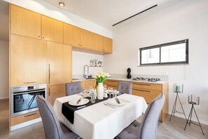 Una cucina moderna con mobili in legno, forno integrato e zona pranzo per quattro, apparecchiata con tovaglia bianca e un vaso di fiori.