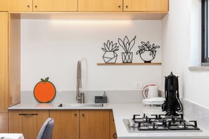 Une cuisine avec des meubles en bois, un évier en acier inoxydable, une cuisinière à gaz et des plantes en pot fixées au mur.