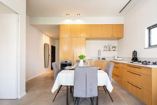 Une cuisine moderne avec des meubles en bois, une table à manger pour quatre personnes et un îlot de cuisine doté d’un évier et d’un plan de travail.
