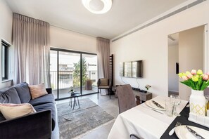 Un soggiorno moderno con un divano, un tavolo da pranzo per due persone, una televisione e un balcone con tende.