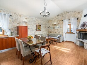A cozy living room with a stone wall, a fireplace, and a dining area with a glass table and chairs. - Casa Antignana with pool in Istria (Tinjan)
