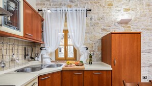 A kitchen with wooden cabinets, a stone wall, a window with white curtains, and a cutting board with food. - Villa Casa Antignana with pool in Tinjan, Istria (Tinjan)