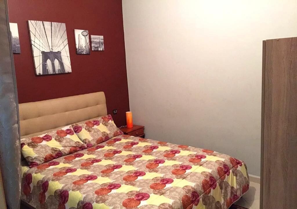 Quarto com cama, mesa de cabeceira e parede com quadros.