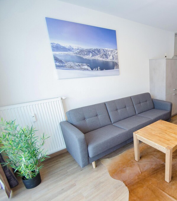 A modern living room with a grey sofa, a wooden coffee table, a potted plant, and a large landscape painting on the wall.
