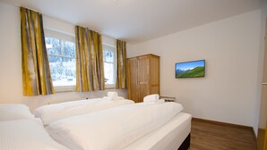 Een hotelkamer met twee bedden, een houten kledingkast, een landschapsschilderij en een raam met gordijnen.