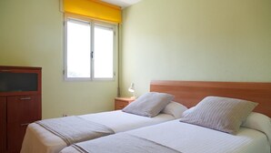 Habitación doble con dos camas, un armario de madera, un escritorio, una lámpara y una ventana con persianas amarillas.