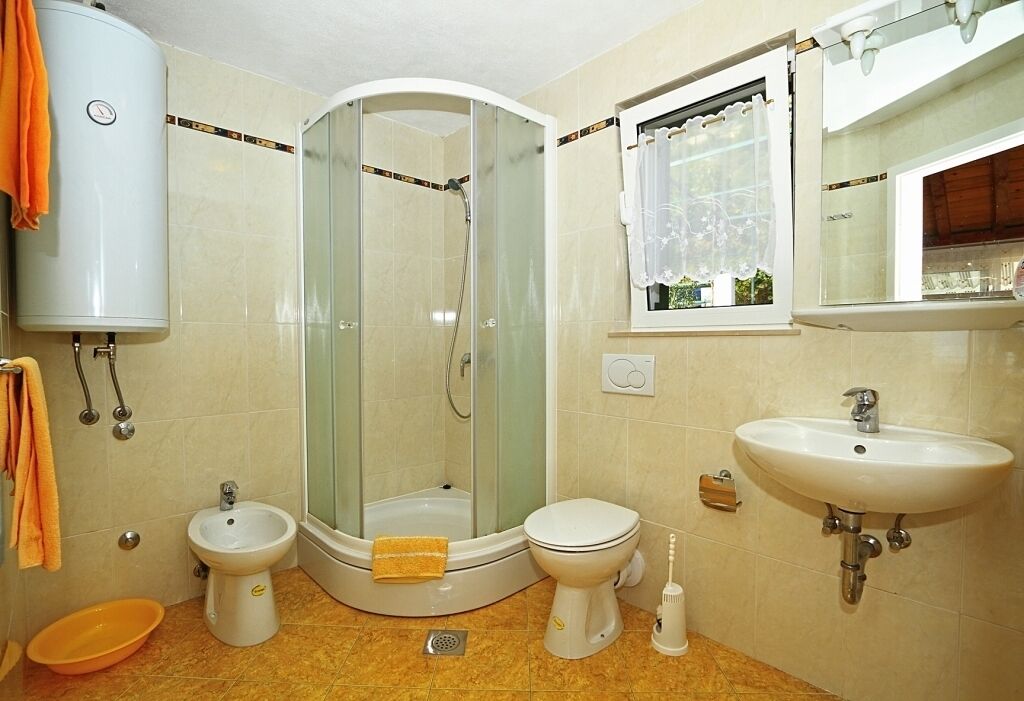Ein Badezimmer mit Dusche, Bidet, Toilette, Waschbecken und einem Fenster mit Vorhang.
