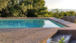 Une piscine dont le bord est recouvert de petits galets, entourée d’une végétation luxuriante et d’un mur de pierre.