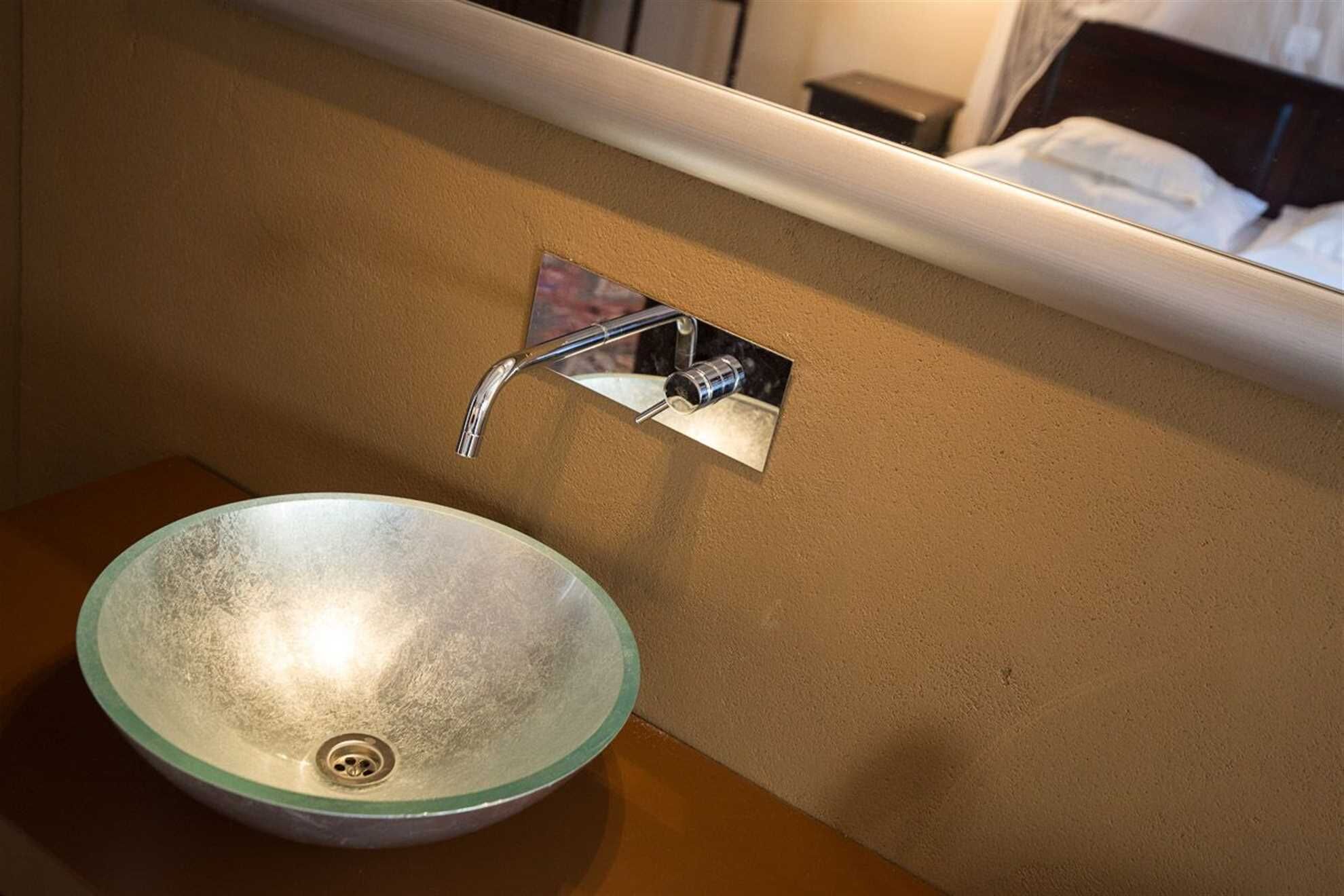 A bathroom with a glass bowl sink and a chrome faucet mounted on the wall.