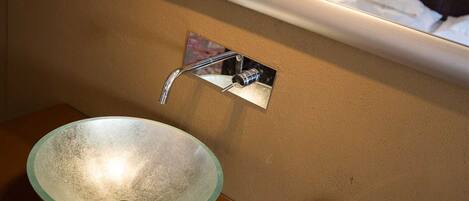 A bathroom with a glass bowl sink and a chrome faucet mounted on the wall.
