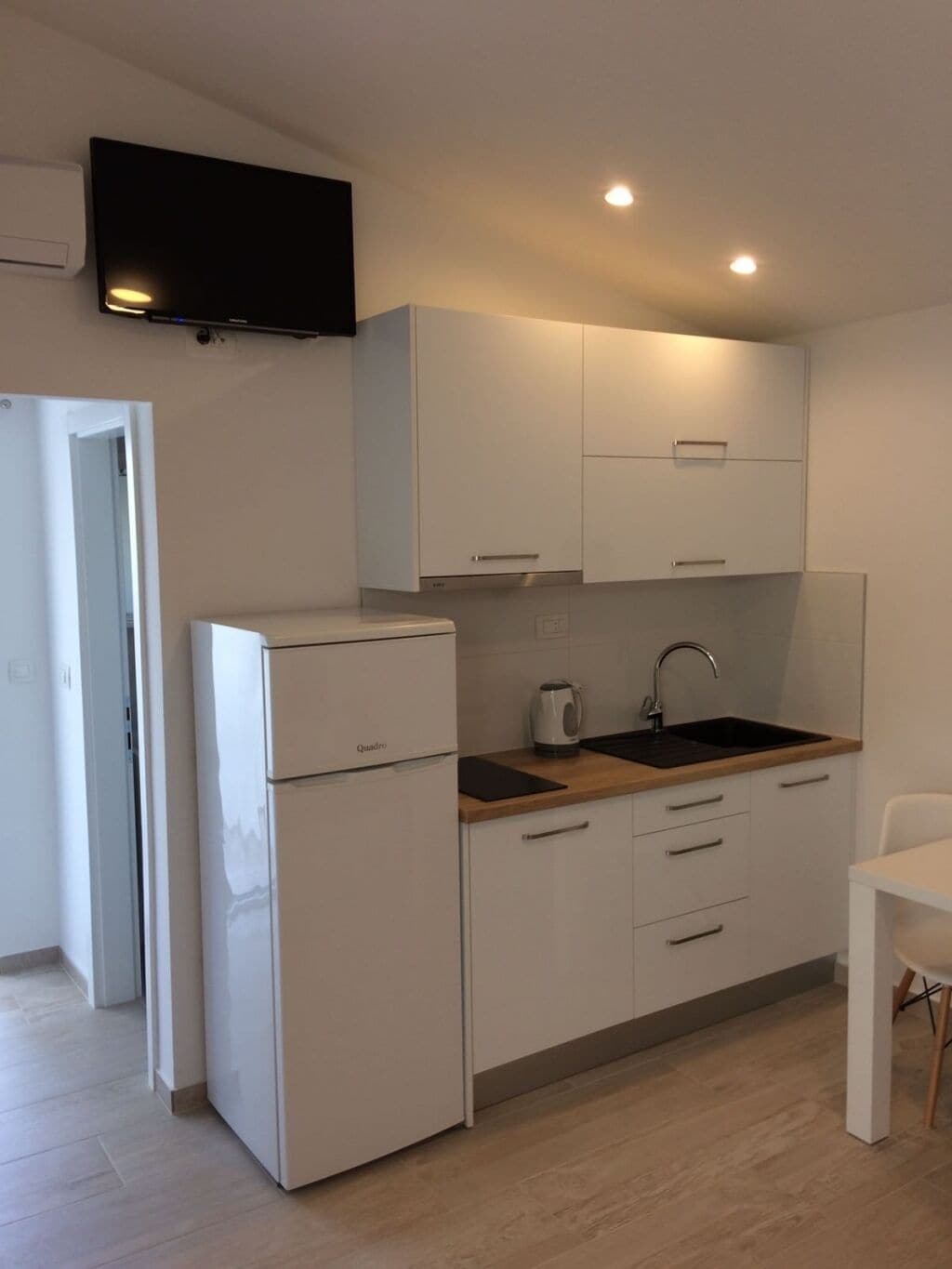 A compact kitchen with white cabinetry, a built-in oven, a sink, and a flat-screen TV mounted above the counter.