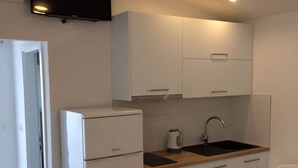 Eine kompakte Küche mit weißen Schränken, einem Backofen, einer Spüle und einem flachbildschirmigen Fernseher, der über der Arbeitsfläche angebracht ist.
