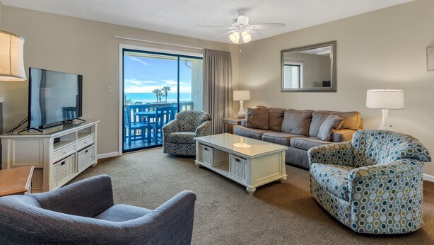 A living room with a television, sofa, armchair, and a view of the beach through a sliding door. - Two Balconies, Walk to the Beach, Pool, Beach Service, Remodeled Bathrooms (Miramar Beach)