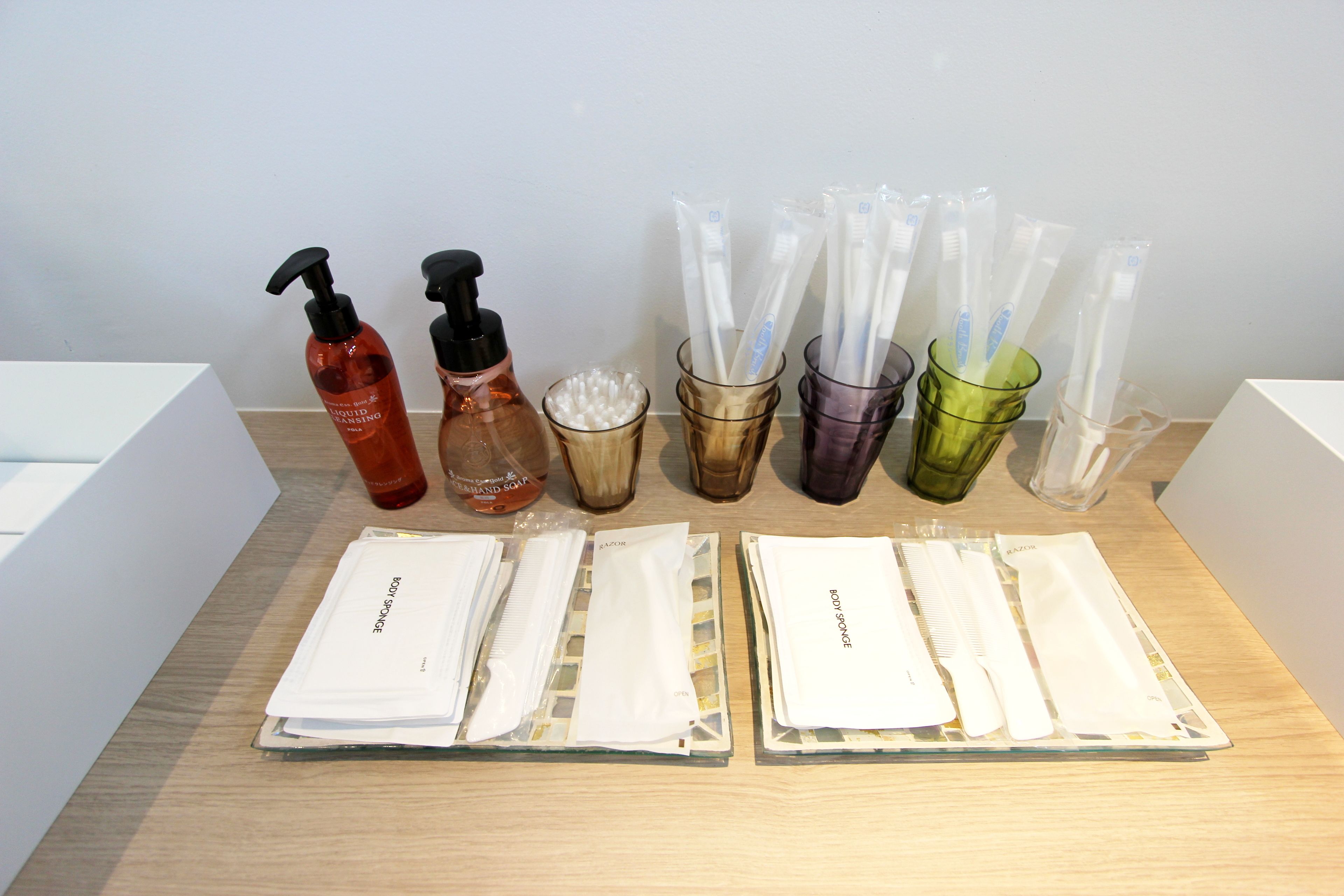 Une table sur laquelle sont disposés divers produits de toilette et articles de soins personnels, notamment des flacons de shampoing, d’après-shampoing et de gel douche, ainsi que des brosses à dents et du dentifrice.