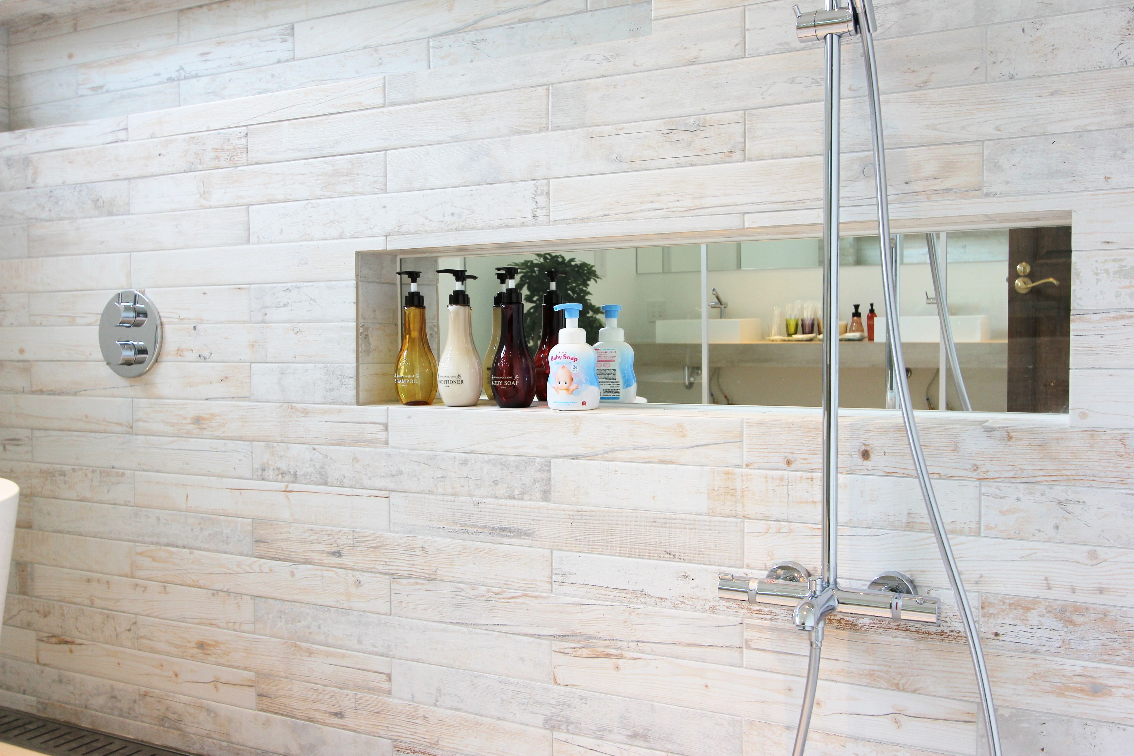 A bathroom with a wooden wall, a glass shelf with toiletries, and a shower.