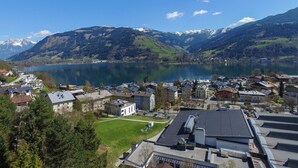 A lakeside town with buildings, a parking lot, and mountains in the background. - Apartment THE GOOD VIEW II - Lake & Mountain view (Zell am See)