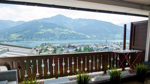 A balcony with a view of a lake and mountains, wooden railing, and potted plants. - Apartment THE GOOD VIEW II - Lake & Mountain view (Zell am See)